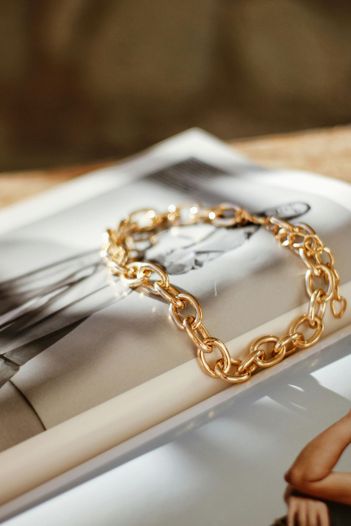 A gold chain bracelet rests on an open fashion magazine with black-and-white photos.